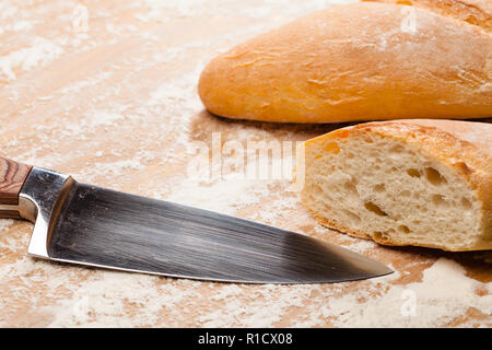 In Scheiben geschnitten sreshly gebackene handwerklichen Baguette (französisches Brot) und Messer auf hölzernen Tisch mit Mehl Stockfoto