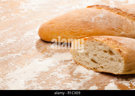 In Scheiben geschnitten sreshly gebackene handwerklichen Baguette (französisches Brot) Auf Holztisch mit Mehl Stockfoto