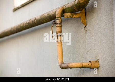 Close-up Detail des Alten schmutzig gelb lackiert Erdgasleitungen mit Schweißnähte und Hahn Ventil befestigt, um graue Hauswand. Sicherheit, Gefahr, alt und Stockfoto