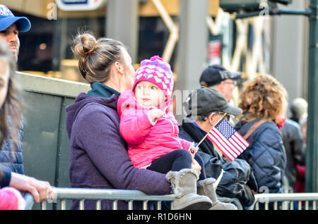 Eine Frau unter den Zuschauern gesehen, die ein Kind während der Parade. Tausende von mehr als 300 Einheiten in den Streitkräften nahmen an der jährlichen Veterans Day Parade. Die Veterans Day Parade statt entlang der 5th Avenue in New York City ehrt den Dienst derer, die in den amerikanischen Streitkräften gedient habe. Stockfoto