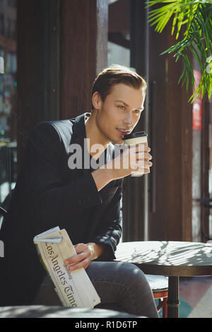 Ein Geschäftsmann, Porträt, er sitzt in einem Café eine Tasse Kaffee mit einer Zeitung. Eine erfolgreiche junge Unternehmer portrait. Stockfoto