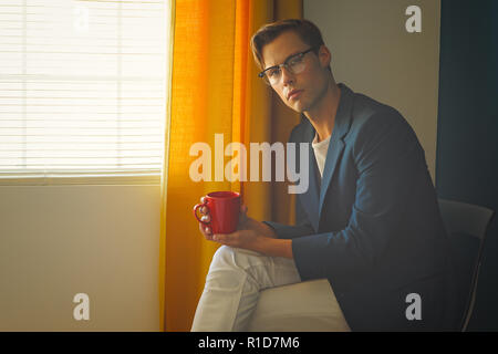 Ein junger Mann, Mann im blauen Anzug und weissen Hosen, trägt ein Paar vintage Gläser, rote Tasse. Einen Men's Vintage Mode Konzept. Stockfoto