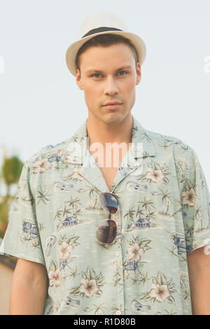Ein schönes männliches Modell im Sommer Shirt outdoor vor blauem Himmel posieren. Er trägt einen weißen Fedora Hut. Stockfoto