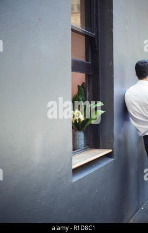 Mann lehnte sich gegen die Wand und Blumen im Fenster. Stockfoto