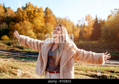 Fröhliches Mädchen mit erhobenen Händen auf dem Feld in warmen Herbst. Stockfoto