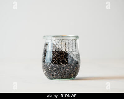 Gesundes Frühstück Konzept und Idee - zwei Farben chia Pudding auf weißen Tischplatte. Glas Glas mit schwarzer Kohle und weiße vegane Milch chia Pudding. Kopieren Sie Platz für Text Stockfoto