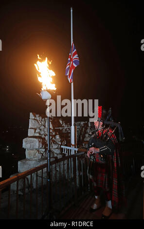 David Danks der Stadt Leeds Pipe Band spielt wie ein Leuchtturm leuchtet in Conisbrough Schloss in South Yorkshire auf das 100-jährige Jubiläum der Unterzeichnung des Waffenstillstandes. Über tausend Beacons, Symbol für das Ende der Finsternis von Krieg und eine Rückkehr in das Licht des Friedens, Leuchten, die über dem Land. Stockfoto