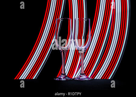 Zwei Sektgläser mit Streifen von bunten Neon Licht hinter Ihnen mit einer LED-Taschenlampe erstellt Stockfoto