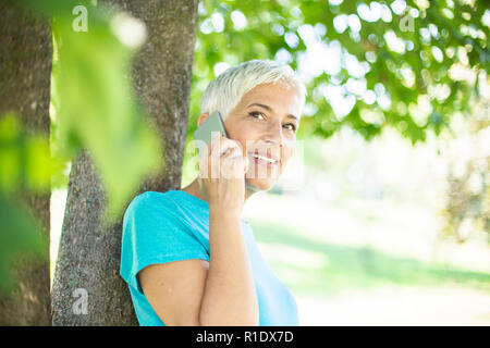 Portrait von sportlichen ältere Frau mit Handy im Park an einem sonnigen Tag Stockfoto