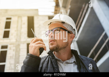 Männliche Leiter Ingenieur tragen weiße Sicherheit hardhat mit Walkie talkie während der Inspektion Baustelle. Entwicklung und Konstruktion Industrie Konzept Stockfoto