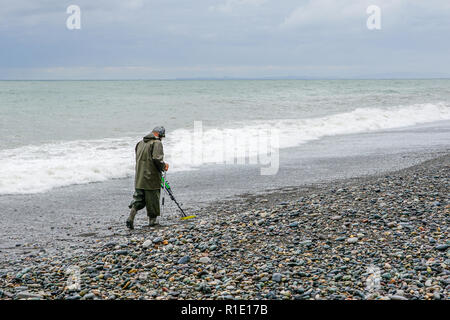 Ein Mann in einem cout mit einem Metalldetektor Spaziergänge am Strand des Schwarzen Meeres, Treasure Hunter Stockfoto