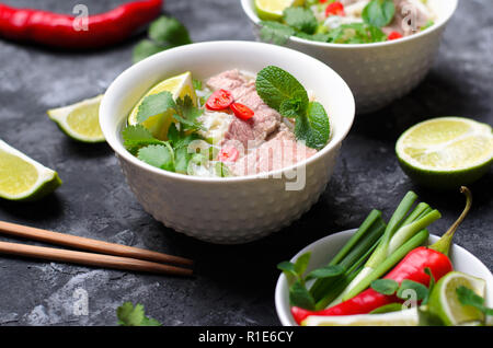 Traditionelle vietnamesische Suppe Pho Bo mit Reis Nudeln, Rindfleisch und Kräutern auf dunklem Hintergrund, asiatische Küche Stockfoto