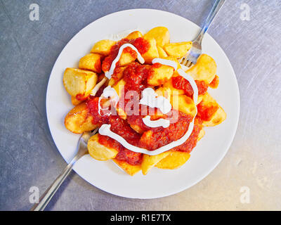 Ein Teil der Patatas Bravas über eine metallische Tabelle. Bratkartoffeln mit würziger Sauce, eine der häufigsten typische spanische Tapas. Stockfoto