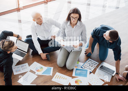 Junge kreative Menschen in modernen Büro. Die Gruppe junger Geschäftsleute gemeinsam mit Laptop. Freiberufler sitzen auf dem Boden. Zusammenarbeit corporate Achievement. Teamwork Konzept Stockfoto