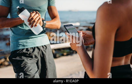 Sportliche Paare stehen im Freien zusammen eine Pause nach der Ausführung. Mann auf seine Armbanduhr, eine Flasche Wasser, während seine Freundin Stockfoto