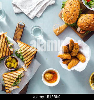 Verschiedene Snacks. Gegrilltes Sandwich mit Nuggets, Salat, Sauce und eingelegte Gurken auf blauen Hintergrund der Ansicht von oben. Outdoor Essen Konzept Stockfoto