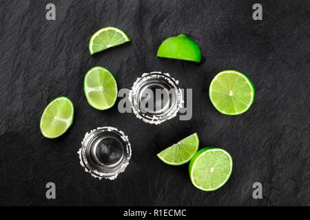 Ein Foto von zwei tequila Schüsse mit vielen Kalk Scheiben, geschossen von oben auf einem schwarzen Hintergrund mit einem Platz für Text Stockfoto