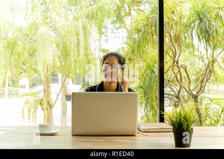 Asiatische Frau legt den Finger auf das Denken der Idee mit Laptop im Coffee Shop. Stockfoto