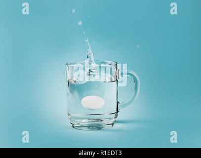 Seitenansicht des löslichen Schmerzmittel Tablette Tropfen im Wasser planschen, ganz klares Glas Schale, auf blauem Hintergrund. Viel Kopie Raum. Stockfoto