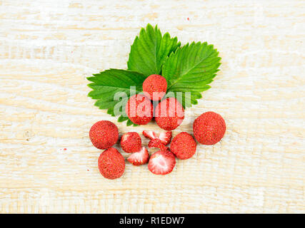 Gefriergetrocknete ganze Stücke von Erdbeeren auf grüne Erdbeere Blatt, gesunden Snack voller Vitamine und Ernährung auf natürliche Holz- Hintergrund. Stockfoto