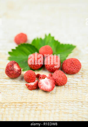 Gefriergetrocknete ganze Stücke von Erdbeeren auf grüne Erdbeere Blatt, gesunden Snack voller Vitamine und Ernährung auf natürliche Holz- Hintergrund. Stockfoto