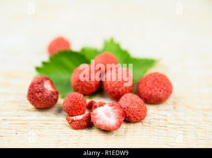 Gefriergetrocknete ganze Stücke von Erdbeeren auf grüne Erdbeere Blatt, gesunden Snack voller Vitamine und Ernährung auf natürliche Holz- Hintergrund. Stockfoto