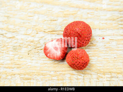 Gefriergetrocknete ganze Stücke von Erdbeeren auf grüne Erdbeere Blatt, gesunden Snack voller Vitamine und Ernährung auf natürliche Holz- Hintergrund. Stockfoto