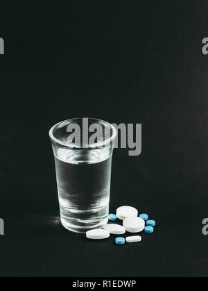 Das Mischen von Alkohol mit Drogen Pillen ist schlecht gefährlich Konzept. Glas Wodka mit Pillen, Tabletten, Drogen auf schwarzen Hintergrund. Stockfoto