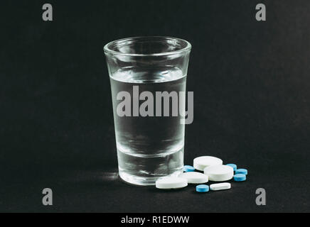 Das Mischen von Alkohol mit Drogen Pillen ist schlecht gefährlich Konzept. Glas Wodka mit Pillen, Tabletten, Drogen auf schwarzen Hintergrund. Stockfoto