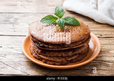 Schokolade Pfannkuchen mit Beeren Marmelade und Minze für Frühstück auf Holz- Hintergrund. Stockfoto