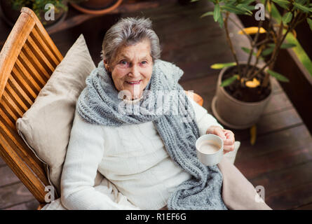 Ein Blick von Oben auf die ältere Frau mit einer Tasse Kaffee sitzen draußen auf der Terrasse. Stockfoto