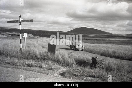 1950, historische, ein Auto auf einer leeren Straße in die karge Umgebung des Snowdonia National Park, Wales geparkt. Ein Schild für Festiniog kann im Bild zu sehen. Stockfoto