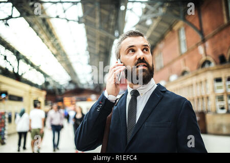 Geschäftsmann mit Smartphone auf dem trian Bahnhof in London, ein Telefonanruf. Stockfoto