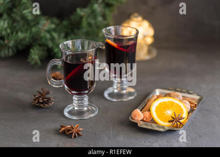 Winter Zusammensetzung. Glühwein in Gläsern auf schwarzen Hintergrund. Tanne Kranz, Lichter, Fach mit Orange, Zimt, Nüssen, Kegel und Gewürze in der Nähe. Stockfoto