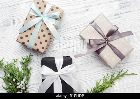 Drei Geschenksets & grüne Zweige auf weißem Holz- Hintergrund. Weihnachten, Neujahr, Boxing Day. Stockfoto