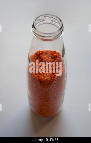 Rohe rote Linsen in Glasfläschchen auf weißem Hintergrund Stockfoto