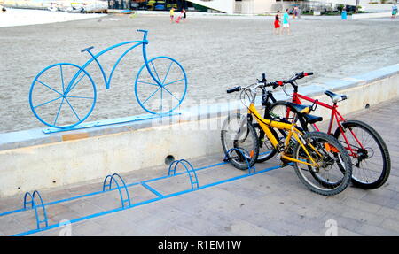 Santiago de la Ribera, Murcia, Spanien - 31. Juli 2018: Fahrräder in einem fahrradständer abgestellt, durch eine moderne markiert schmiedeeiserne Skulptur von einem Fahrrad, mit dem Stockfoto
