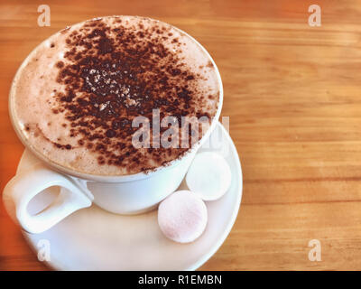 Trinken Sie heiße Schokolade mit Milch Latte Schaum gekrönt mit Marshmallow aus weisser Keramik Schale auf holztisch Hintergrund. Fit mit gesunder Milch trinken wi Stockfoto