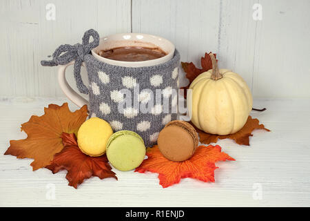 Heißer Kakao trinken in Becher mit grauen Polka Dot Pullover und Makronen auf Herbst Blätter und weiß getünchte Holz Stockfoto