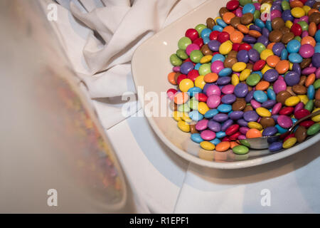 Schüssel mit Smarties zu einem Kinder Partei auf einem weißen Tuch mit Reflexion. Horizontale. Platz für Text. Stockfoto