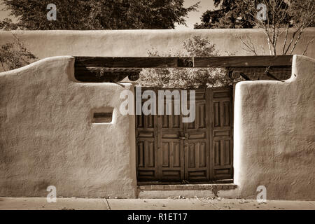 Eine bezaubernde Aussicht auf eine Adobe Wand- und Vintage Holztüren mit roten Blättern auf Bäume im Herbst Innenhof im historischen Viertel von Santa Fe, NM Stockfoto