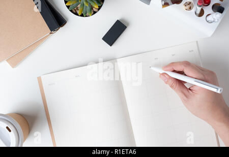 Blick von oben auf die Hand schreiben auf Kalender öffnen Routenplaner für business Auflösung mit modernen Büro- und Schreibwaren, und nehmen Sie die Kaffeetasse auf weißem Schreibtisch in Offi Stockfoto