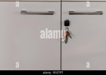 Schlüsselbund hängen aus dem Schlüsselloch eines weißen Schrank mit Metallgriffen Stockfoto