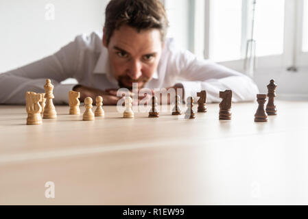 Geschäftsmann sein Kopf lehnte sich auf seinen Handflächen auf Büro Schreibtisch in Weiß gegen Schwarz Schachfiguren auf hölzernen Schreibtisch mit Kopie Raum angeordnet. Stockfoto