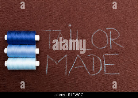 Blauem faden Spulen in der Nähe von maßgeschneiderten Text mit Kreide auf braunem Material geschrieben Stockfoto