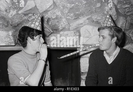 1970 s, historischen, einer Partei, LA, zwei junge Männer mit Party Hüte oder Hütchen auf dem Kopf, Blasen Papier Streamer, Los Angeles, USA. Stockfoto