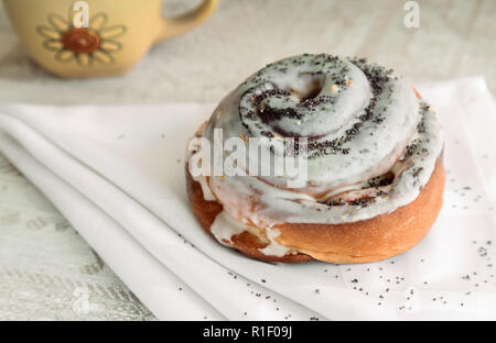 Auf der Tabelle auf einer Serviette ist eine appetitliche Brötchen, mit Glasur und Mohn abgedeckt. Stockfoto