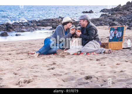 Nettes Paar viel Spaß beim romantischen Picknick im Freien am Strand mit dem besten Freund Hund zusammen mit Ihnen. Freundschaft und Partnerschaft Konzept für Alternativ Stockfoto
