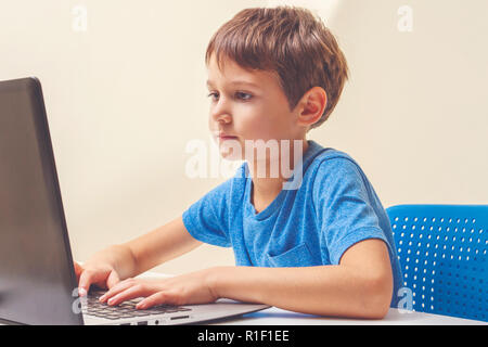Konzentrierte Junge am Schreibtisch mit Laptop sitzen und Hausaufgaben machen. Stockfoto