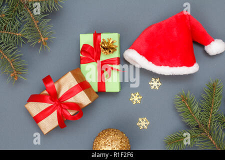 Weihnachtsdekoration. Geschenkboxen, Santa's Hut, Spielzeug, Ball, dekorative Schneeflocken und natürlichen Tannenbaum Äste auf grauem Hintergrund. Ansicht von oben. Weihnachten g Stockfoto